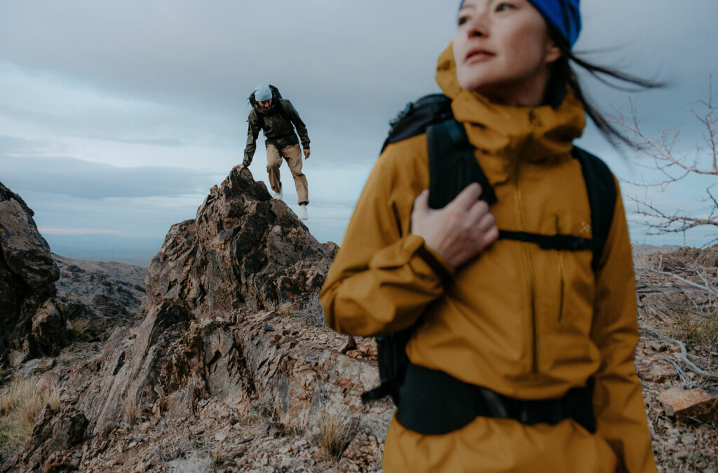 Two people hiking on a rocky terrain under a cloudy sky.