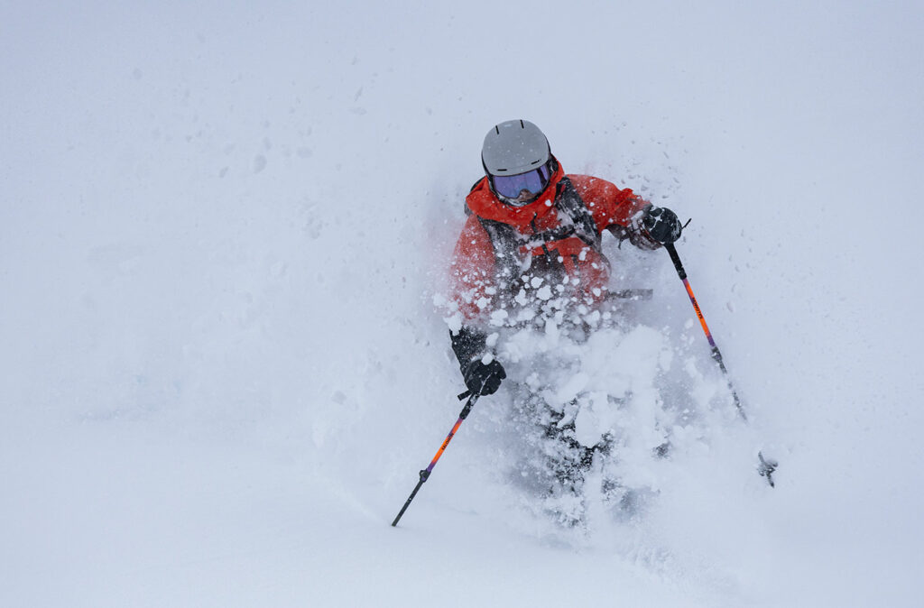 Skier in a red jacket and helmet carving through deep snow.